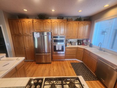 Kitchen with tall oak cabinets, stainless steel French-door fridge, and built-in double ovens along the wall. The foreground shows a gas cooktop island.