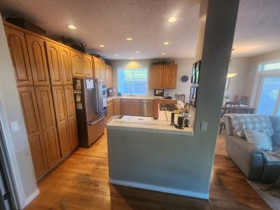 Cozy kitchen with tall wooden cabinets, stainless steel refrigerator, and a tile-topped island under recessed lighting.
