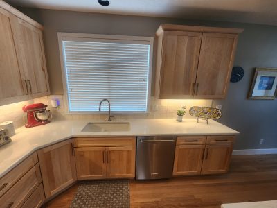 Kitchen with light wood cabinets and white counters, sink under a window with blinds, red stand mixer on the counter.