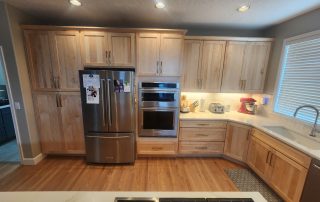 Modern kitchen with light wood cabinets, stainless fridge and wall ovens along a U-shaped counter.