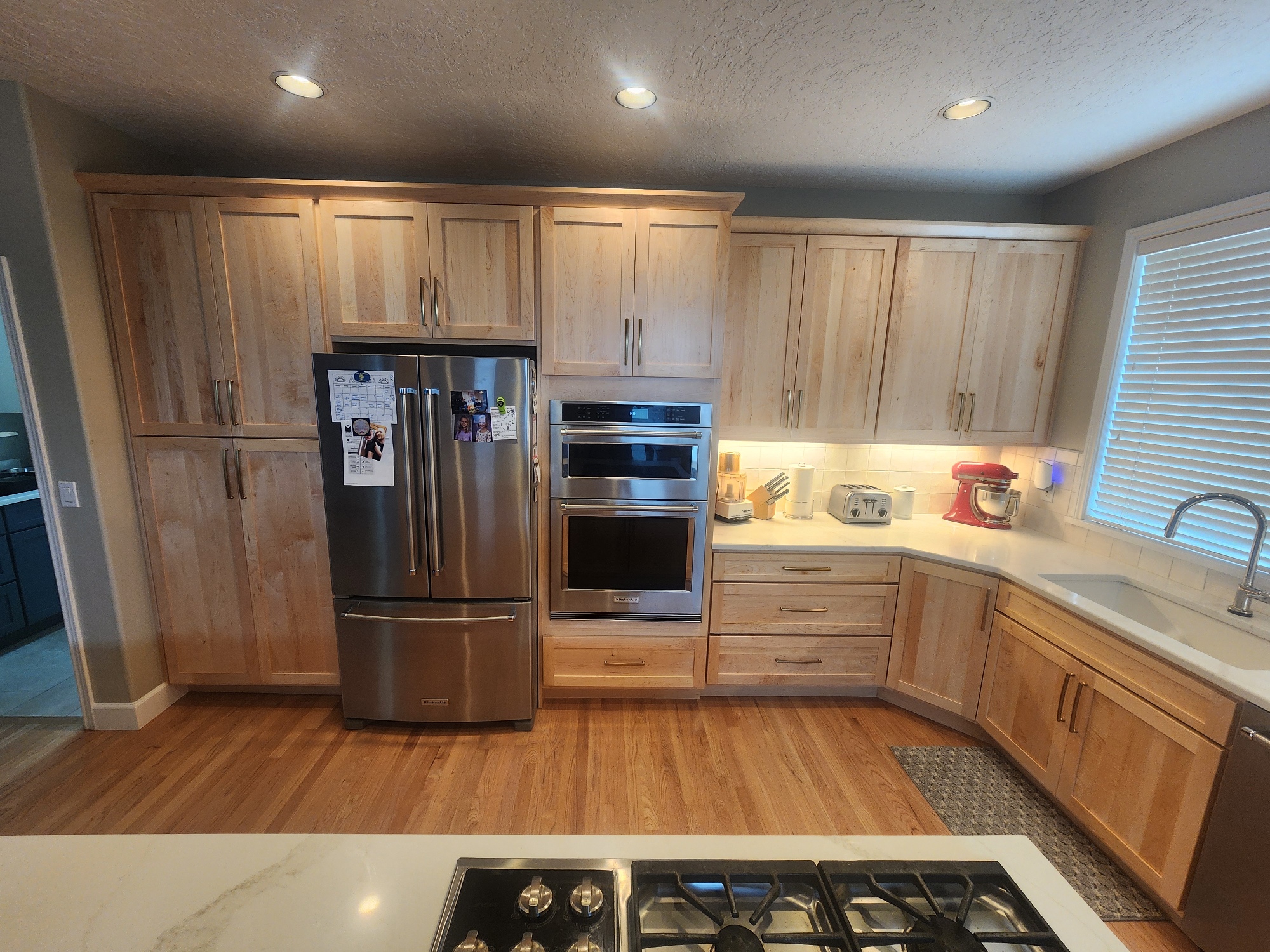 Modern kitchen with light wood cabinets, stainless fridge and wall ovens along a U-shaped counter.