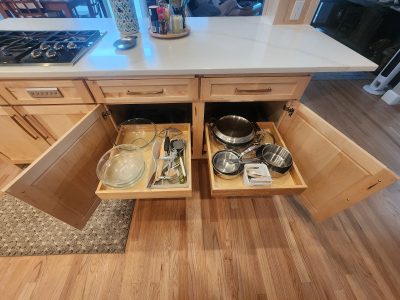 Kitchen island with open drawers showing pots, pans, and utensils in a homey kitchen setup.