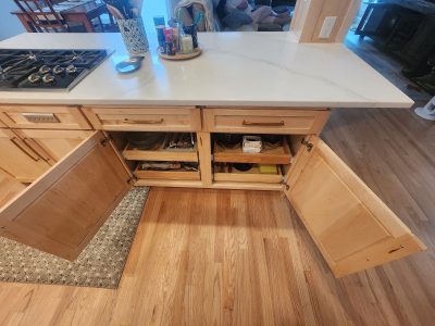 Kitchen island with white marble countertop, gas stove on left, and open drawers showing pots and pans.