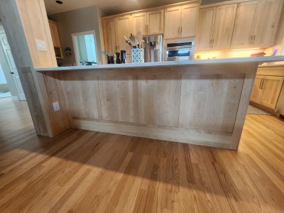 Oak kitchen with a long raised bar in the foreground, light wood cabinets, and stainless steel appliances in the back.