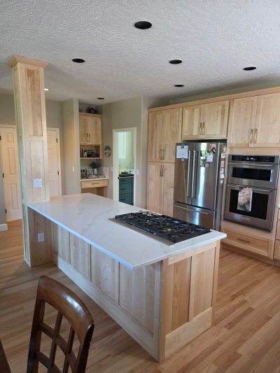 Bright kitchen with light wood cabinets, white marble island, and stainless steel fridge and ovens; gas cooktop on island.