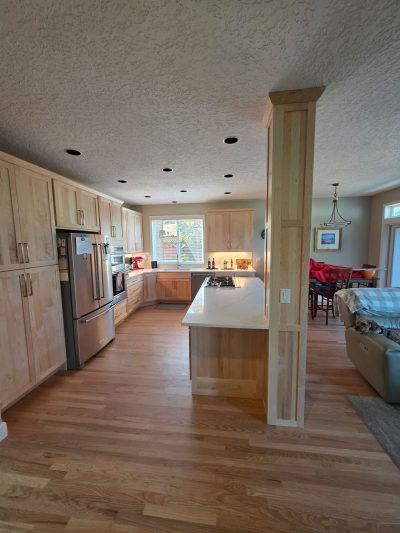 Kitchen with light wood cabinets and island; ceiling shows several round cutouts for recessed lighting awaiting installation.