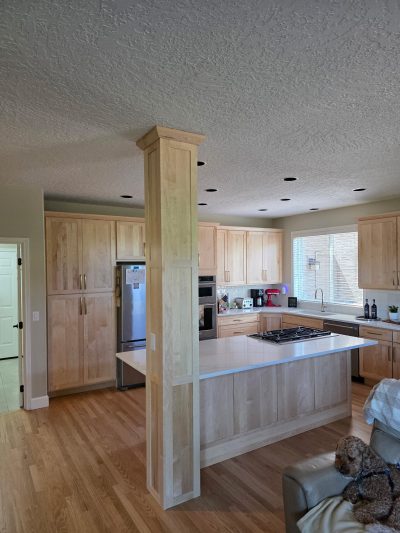 Open kitchen with light wood cabinets and a central island; a small dog relaxes on a beige sofa near the counter.