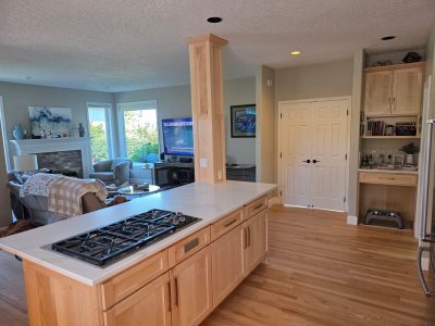 Open-concept kitchen with a marble-topped island and a gas range, light wood cabinets, and a living room with a fireplace in the background