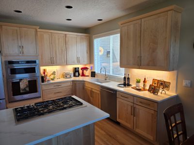 Kitchen with light wood cabinets, white countertops, and a large island gas range; lemon-yellow lighting under-cabinet glow visible.